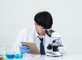 retrato asiático hombre estudiante científico vistiendo un médico vestido en el laboratorio mirando mano a químico. causado por mezcla reactivos en científico investigación laboratorios con prueba tubos y microscopio en el mesa foto