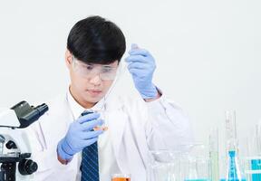 Portrait asian man student scientist Wearing a doctor gown in the lab looking hand at chemist. caused by mixing reagents in scientific research laboratories with test tubes and microscope on the table photo