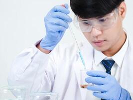 retrato asiático hombre estudiante científico o médico Mira mano participación reactivo mezcla laboratorio en Ciencias investigación laboratorio con prueba tubos de varios Talla en laboratorio química laboratorio blanco antecedentes foto