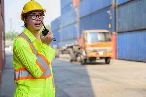 Asian man worker talking on walkie talkie to driver for control loading containers box at cargo shipping yard photo