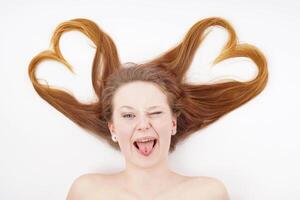 joven mujer con pelo formando corazón forma y parpadeo mientras pega fuera lengua foto