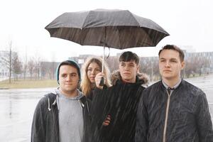 grupo de joven urbano Adolescente amigos debajo uno paraguas foto