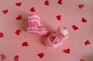 Knitted pink booties baby socks on pink background with hearts photo