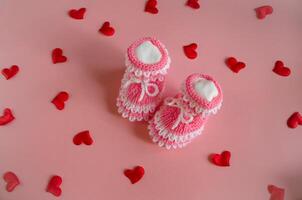 Knitted pink booties baby socks on pink background with hearts photo