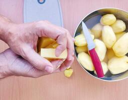 Close up of man holding and peeling potato. Hands cutting potatoes at kitchen to prepare a recipe. photo