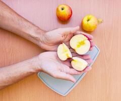 Close up male hands cut an apple into slices. Top view of preparing fruits over kitchen table. photo