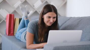 online Einkaufen, Kauf von heim, Anerkennung Karte, online speichern. glücklich Frau Lügen auf das Couch und wählen ein Produkt im das online Geschäft mit ein Laptop video