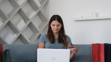 Online shopping, Buying from home, Credit card, Online store. Portrait of a girl who sits on the couch at home and makes an online purchase using a laptop video