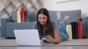 Online shopping, Buying from home, Credit card, Online store. Woman lying on the floor near the sofa at home makes an online purchase using a credit card and laptop video