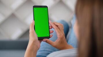 Rear view of woman in modern room sitting on couch using phone with green screen mockup Chroma Key with trackpoints surfing internet Viewing content Blogging. One click 4K video