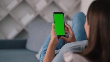 achterzijde visie van vrouw in modern kamer zittend Aan bankstel gebruik makend van telefoon met groen scherm mockup chroma sleutel met trackpunten surfing internet video