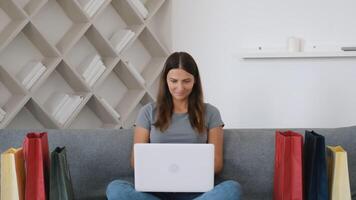 Online shopping, Buying from home, Credit card, Online store. Portrait of a happy girl who sits on the couch at home and selects goods from an online store using a laptop video