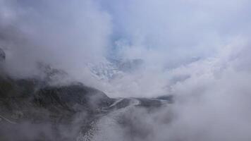 Mountains fog snow-covered peaks wild terrain aerial view. Mountains fog embodying wild nature's beauty Clouds blanket rugged mountains fog Capturing essence of untouched majestic nature. video