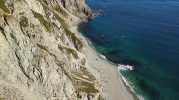 aereo. ecco il travolgente vista di un' soleggiato mantello, definito di suo degno di nota scogliere e abbracciato di montagna creste, prospiciente il incontaminato blu mare e intatto natura video