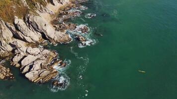 Wild rocky cliffs by sea aerial view by drone top view Cliffs bask bright sun sea's beauty beneath. Sea waves crash against cliffs nature's grandeur Majestic views untouched wilderness. video