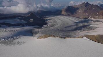 aéreo ver glaciar talla mediante montañas la tierra obra maestra glaciar en invierno paisaje refugio para tranquilidad del Norte estética. en medio de nubes glaciar revela la tierra escabroso intacto belleza. video