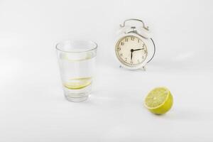 Glass of water, lime and alarm clock on a light background. Space for text photo