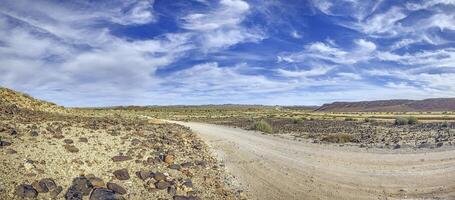 Panoramic picture over a gravel road through the desert like steppe in southern Namibia under a blue sky photo