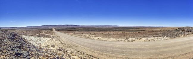 panorámico imagen terminado un grava la carretera mediante el Desierto me gusta estepa en del Sur Namibia debajo un azul cielo foto