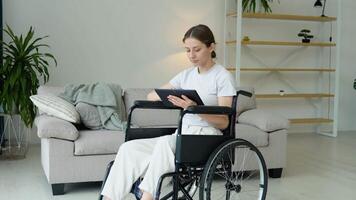 Jeune femelle pigiste est travail dactylographie dans tablette séance dans fauteuil roulant à maison. loin travail concept video
