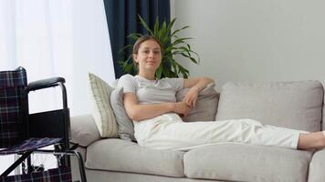 Portrait of young woman with wheelchair looking at camera in living room video