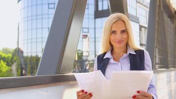 portrait de une sur de soi 50 ans femme dans une affaires costume avec les documents dans de face de une moderne Bureau bâtiment video