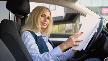 Portrait of a confident woman sitting in a car with documents in a business suit near a modern office building video