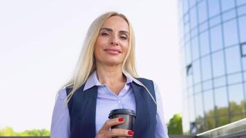 mayor mujer de negocios en pie fuera de un moderno corporativo edificio con café taza. paisaje urbano antecedentes video