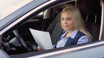 Portrait of a confident 50 years woman sitting in a car with documents in a business suit near a modern office building video