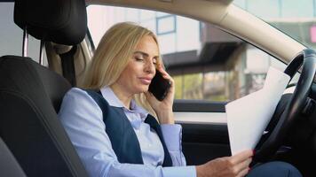 A confident 50 years woman speaks on the phone sitting in a car in a business suit near a modern office building video