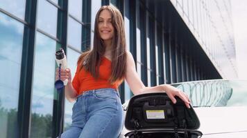 A girl stands with charger near her electric car video