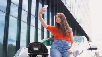 mujer tomando un selfie mientras cargando un eléctrico coche cerca un centro comercial video