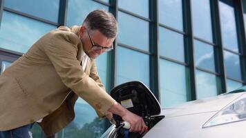 atractivo mayor hombre enchufar en cargando cable a a eléctrico vehículo video