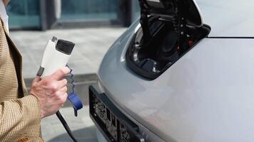 Unrecognizable senior man disconnects charging cable to electric vehicle. Male hand unplugs power connector into EV car and charges batteries video