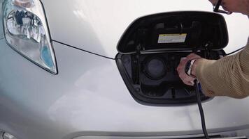 senior Mens verbreekt de verbinding opladen kabel naar elektrisch voertuig. mannetje hand- haalt de stekker uit het stopcontact macht connector in ev auto en kosten batterijen video