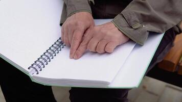 Sénior aveugle homme séance sur banc dans ville parc et en train de lire une braille livre video