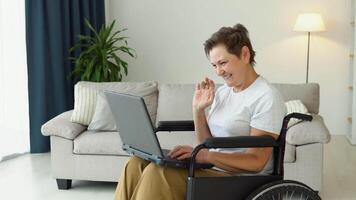 sorridente maduro 50. anos mulher dentro cadeira de rodas conversando em social redes às lar. feliz Mais velho pensionista rede surfar em formação video