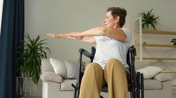 Mature 50 yers woman is spreading her arms in different sides in wheelchair. Training, sport, recovery and lifting, stretching exercise at home video