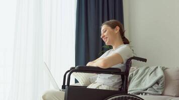 sorridente giovane donna nel sedia a rotelle chat su sociale reti a casa. contento ragazza ragnatela fare surf informazione video