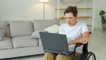 maduro 50 años hembra persona de libre dedicación es trabajando mecanografía en ordenador portátil sentado en silla de ruedas a hogar. distante trabajo concepto video
