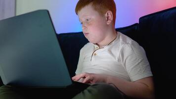 Computer addicted teen boy looking at the notebook screen pressing the keyboard. Teenager using laptop at night time video