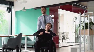 Young man pushing wheelchair with colleague in the office. Support and inclusivity video