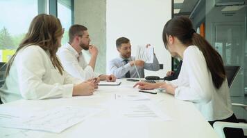 A group of young male and female office employees sitting and discussing on a project in a conference or board room meeting. Businessman discussing work with team in boardroom video