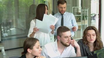 A group of young male and female office employees sitting and discussing on a project in a conference or board room meeting video