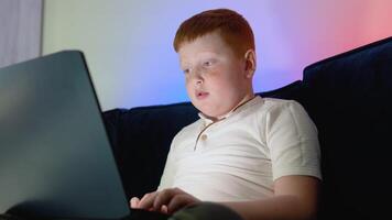 Computer addicted teen boy looking at the notebook screen pressing the keyboard. Teenager using laptop at night time video