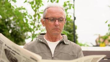 Senior man in glasses reading newspaper in the park. Active retirement video