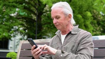 A portrait of an elderly person using a mobile phone, holding device, text messages, surfing on the internet and using the application video