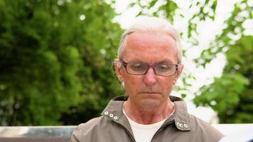 Senior man reading book sitting on bench in park video