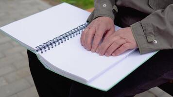 Senior blind man sitting on bench in city park and reading a braille book video