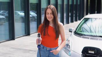 A girl stands with charger near her electric car video